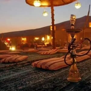 Desert camp at dusk with floor cushions, lanterns and a shisha pipe