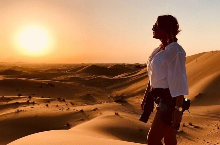 Woman watching sunrise over Dubai desert dunes during morning safari