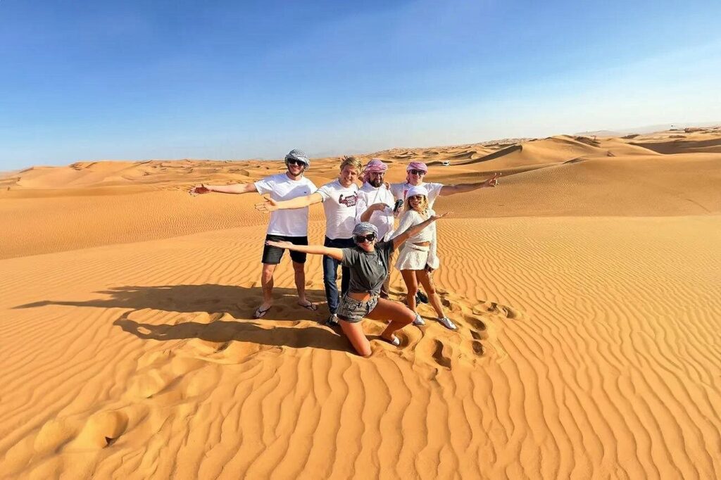 Happy group of tourists posing in the middle of golden sand dunes during a morning desert safari in Dubai.