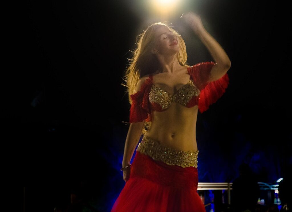 Belly dancer performing in a traditional red costume under spotlight during the evening Dubai desert safari entertainment show.