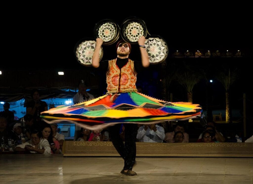 Tanoura dancer spinning in a colorful traditional costume during the night cultural show at Dubai desert safari camp.