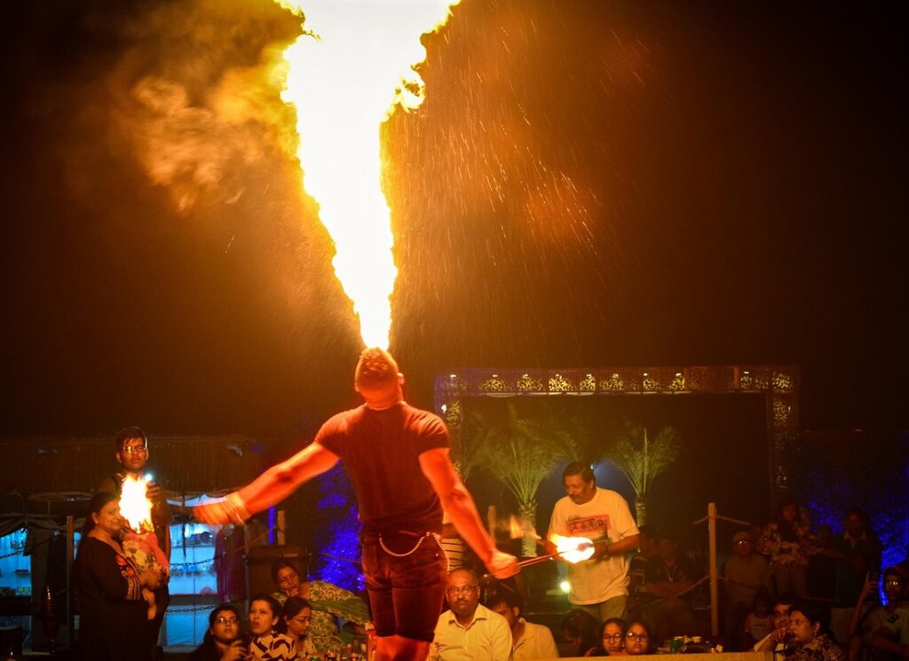 Performer breathing fire during a dramatic fire show at a Dubai desert safari campsite with amazed audience watching.