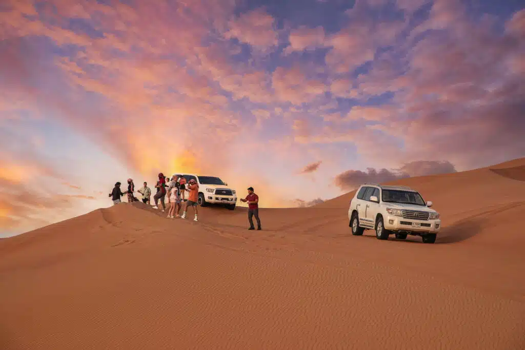 Tourists enjoying sunset desert safari in Dubai with 4x4 Land Cruisers on sand dunes