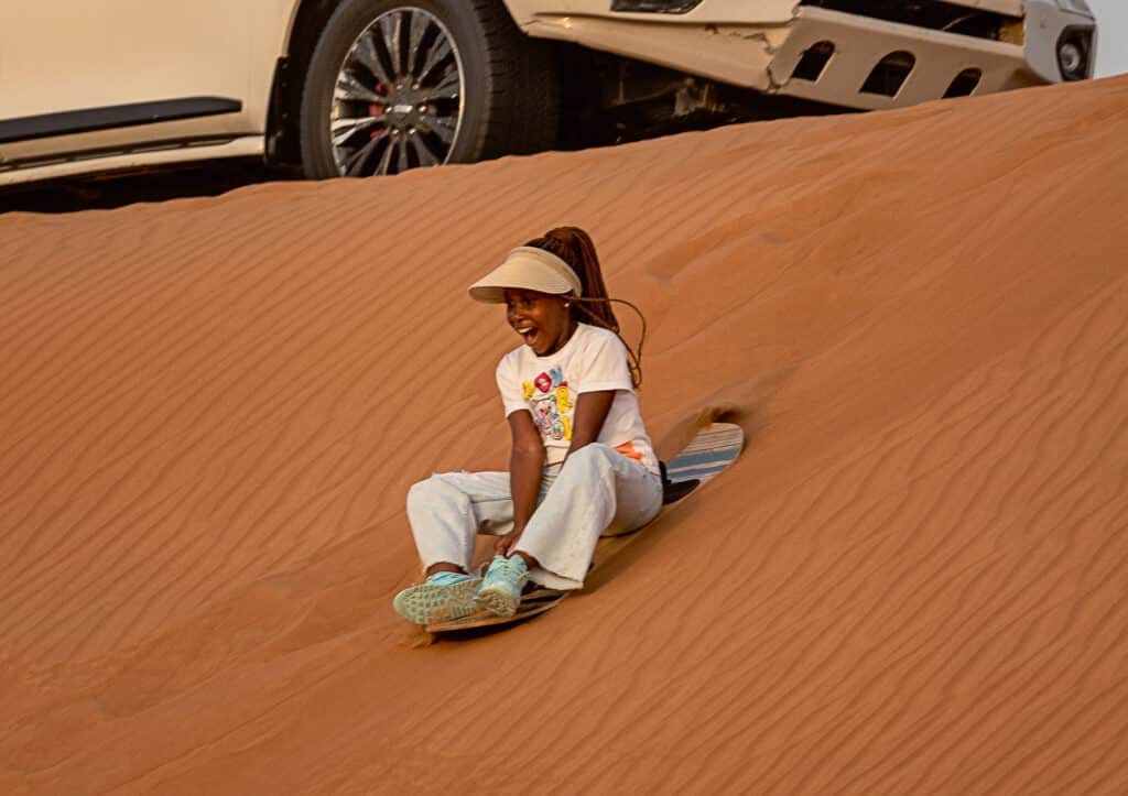 Girl in a sun visor sandboarding down a red dune
