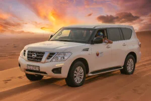 White Nissan Patrol 4x4 on desert sand under a pink and orange sunset sky