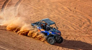 Blue dune buggy speeding across red sand with dust trailing behind