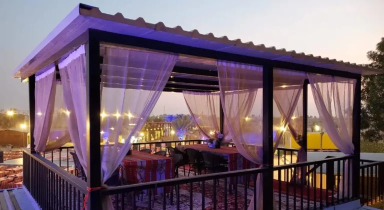 Glass-walled cabana with white curtains and a set table at dusk