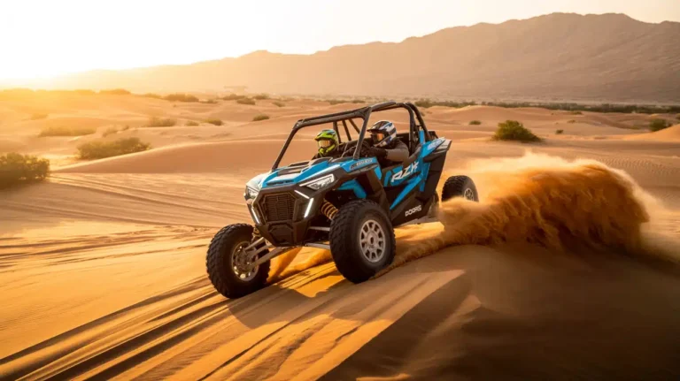 Blue side-by-side buggy driving across a dune with sand spraying behind it