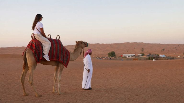 Woman riding a camel beside a guide in white dress in the desert