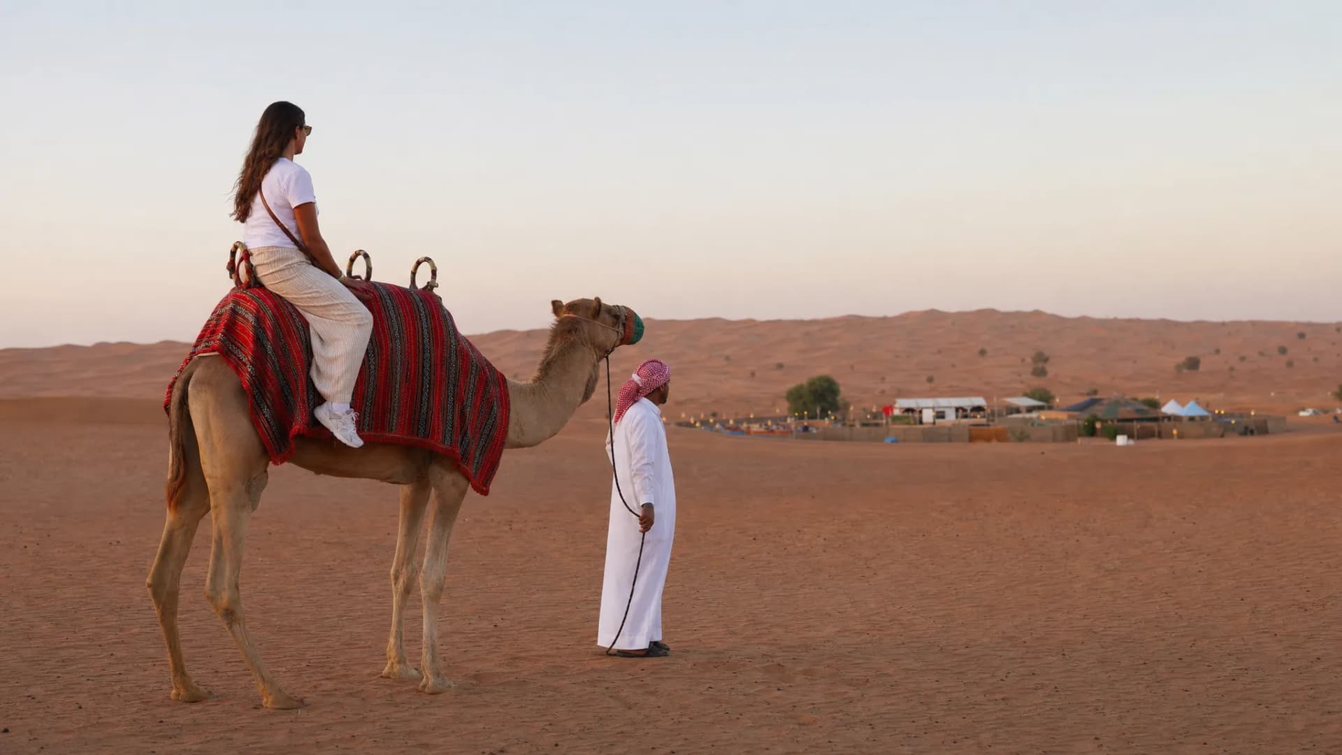 Woman riding a camel beside a guide in white dress in the desert