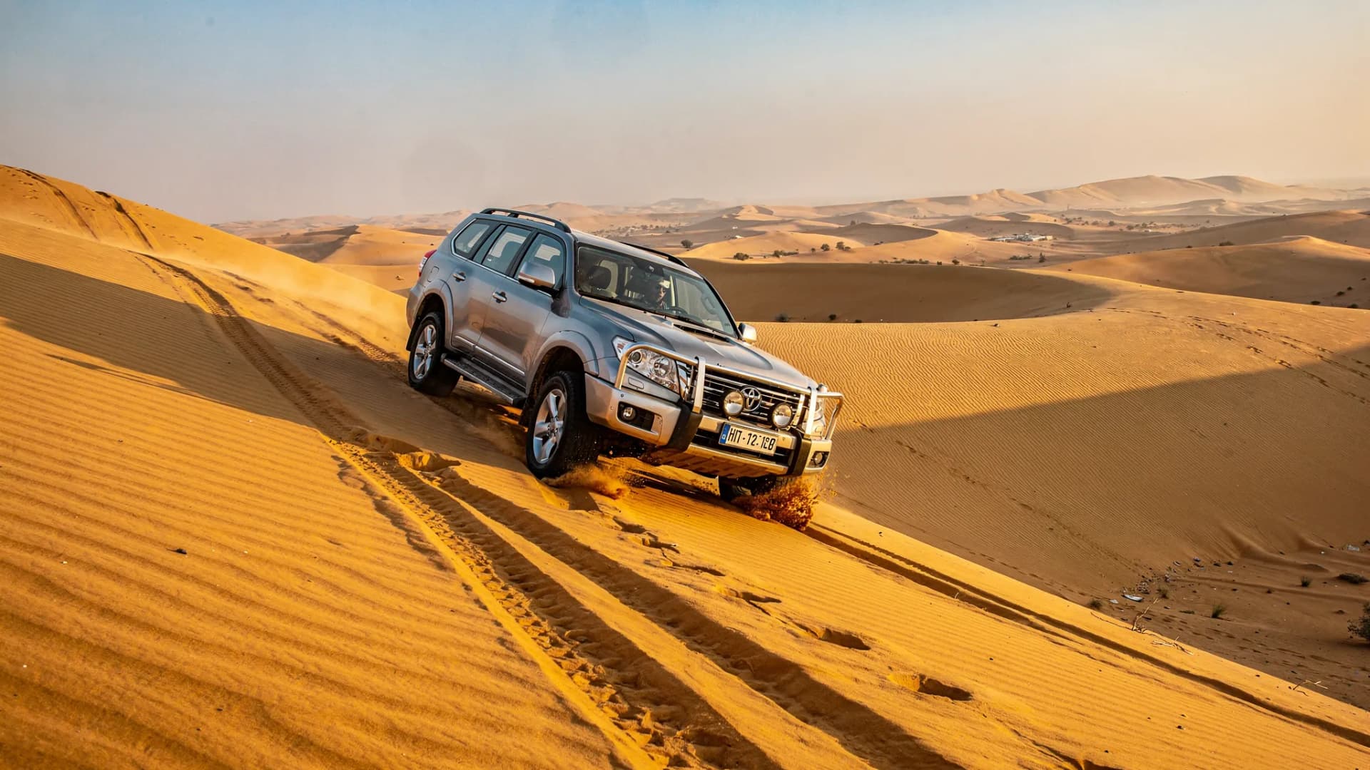 Silver SUV descending a sand dune with tire tracks behind it